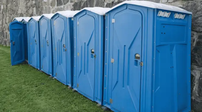 Row of blue portable toilets lined up on grass against a stone wall for event sanitation in Staten Island, NY
