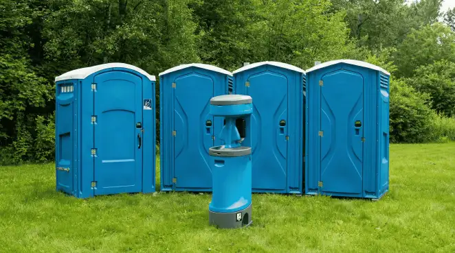 Four blue portable toilets and a matching hand washing station on grass near trees, a common sight at local outdoor events in Staten Island, NY