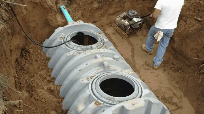 Septic tank installation showing a technician compacting soil around a new poly septic tank in an excavation pit in Staten Island, NY